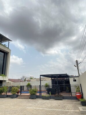A modern building with a covered outdoor area, potted plants, and a paved walkway. - 2-Bedroom Apartment in Quaint Accra with Cool ACs Near Airport (Accra)