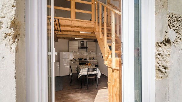 Et køkken med træbjælker, et spisebord med stole og en trappe til en etage ovenover.