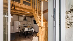 Et moderne køkken med træbjælker, et spisebord med stole, og en trappe til et opholdsrum.