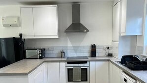 A modern kitchen with white cabinetry, a stainless steel range hood, a microwave, an oven, and a dishwasher. - Gatwick 3 Bed Parking (Surrey)