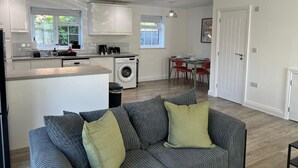 A modern kitchen with a central island, a dining area with a table and chairs, and a living room with a sofa and cushions. - Gatwick 3 Bed Parking (Surrey)