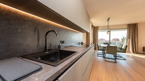 A modern kitchen with a dark countertop, a sink, and a dining area with a table and chairs. - Villa Suton u Zatonu Zadarvillas (Nin)