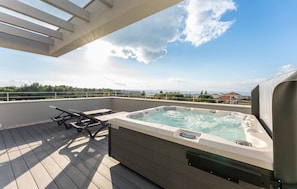 Ein Whirlpool auf einer Holzterrasse mit Blick auf das Meer und Gebäude in der Ferne.