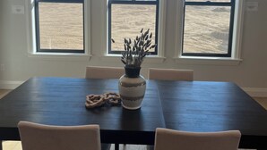 Ein Essbereich mit einem dunklen Holztisch, beigen Stühlen, einer Vase mit Pflanzen und einer Pendelleuchte.