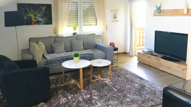 Olohuoneessa on harmaa sohva, kaksi valkoista sivupöytää, televisio ja kattotuuletin.