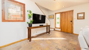 Ein Wohnzimmer mit Flachbildfernseher auf einem Holzboden, einer Topfpflanze und einer großen Holztür.