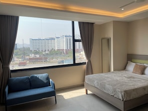 Una habitación de hotel con cama, una silla, un ventanal grande y un ventilador de techo.