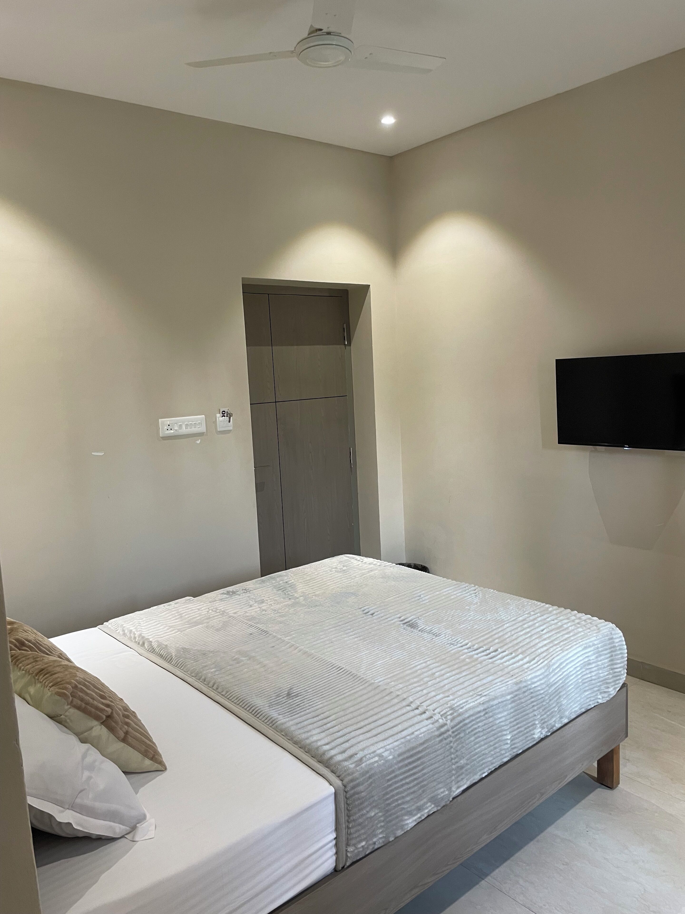 A bedroom with a bed, a ceiling fan, a TV mounted on the wall, and a door.