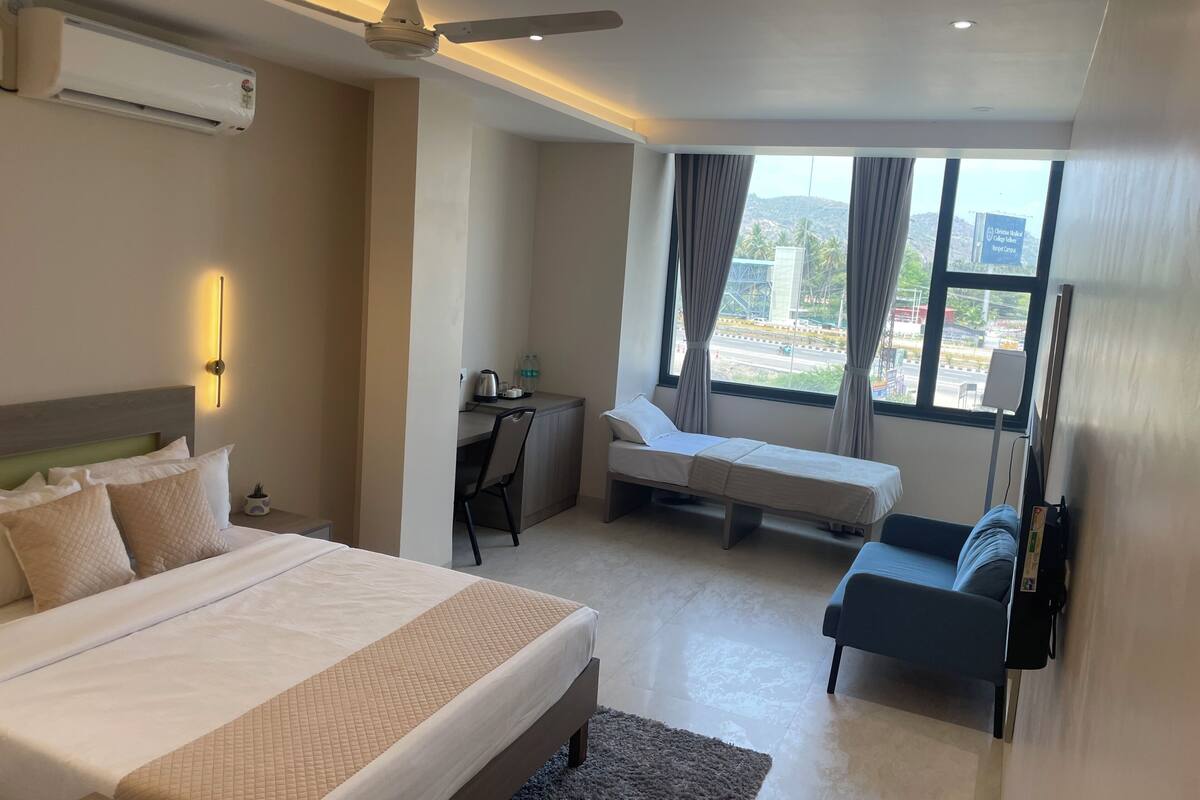 A hotel room with a bed, a desk, a small sofa, and a view of the outside.
