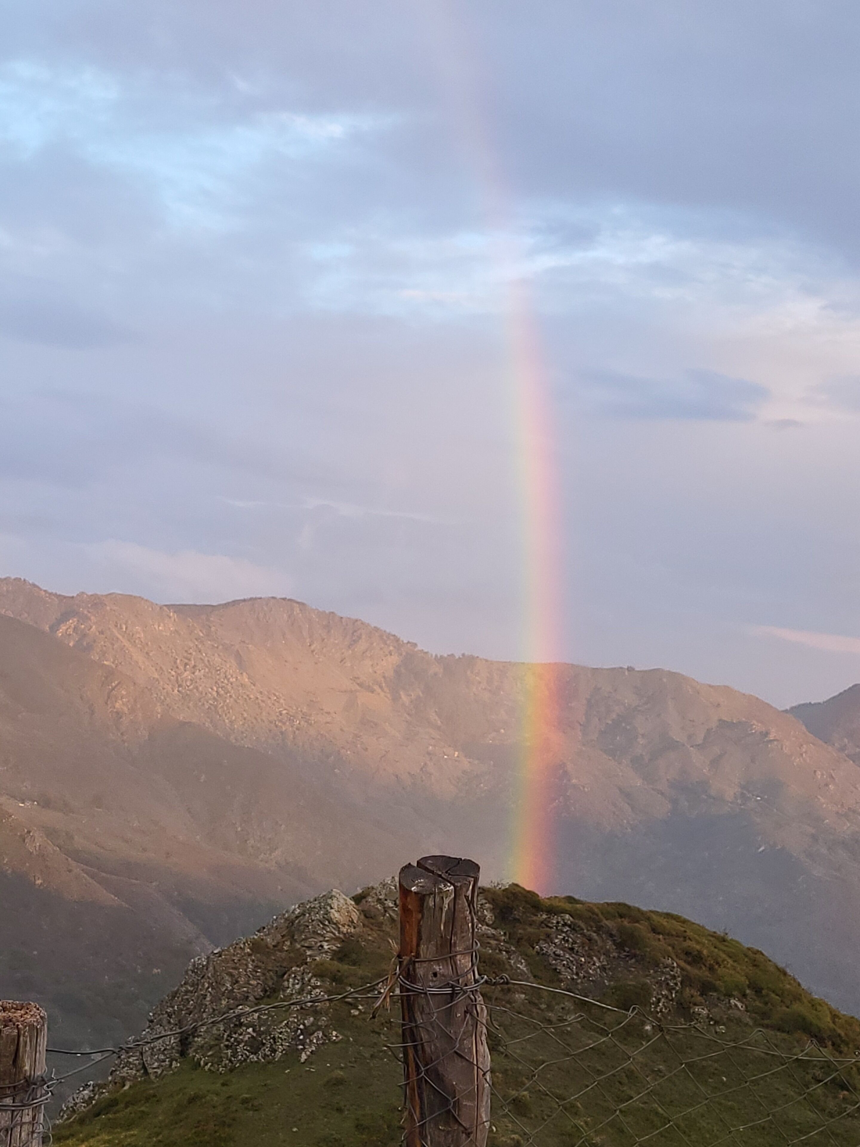 A mountain landscape with a rainbow and a wooden fence.