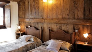 Quarto com duas camas de madeira, cada uma com mesa de cabeceira e luminária. As paredes são de painéis de madeira, e há uma janela no lado esquerdo.