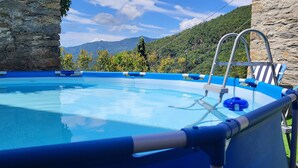 Piscina com borda de vidro, rodeada por muros de pedra e vista para montanhas.