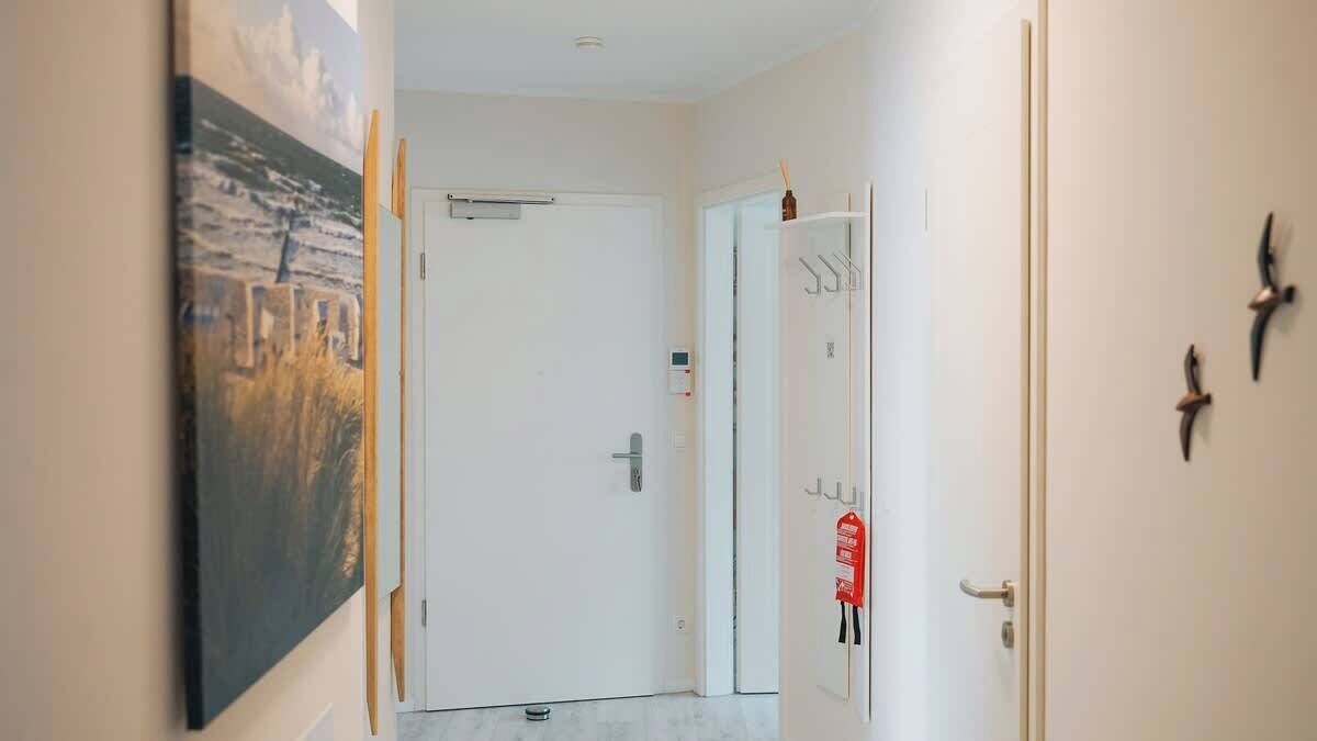 Un couloir avec une porte blanche, un tableau sur le mur de gauche et un extincteur sur le mur de droite.