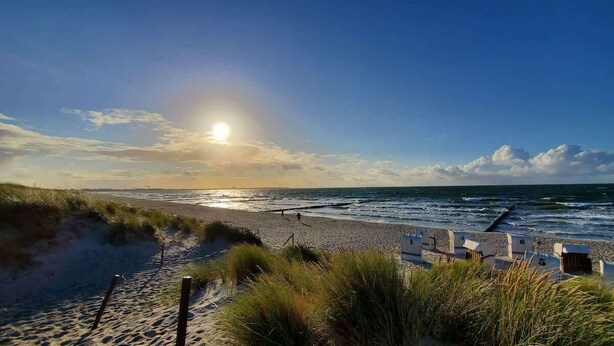 Ein Strand mit blauem Himmel, der Sonnenaufgang oder -untergang, und ein Sandweg zu Liegestühlen.