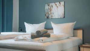 Ein ordentlich bezogenes Bett mit weißen Leinen und gerollten Handtüchern, ein Holz-Kopfteil und ein an der Wand befestigtes Kunstwerk.