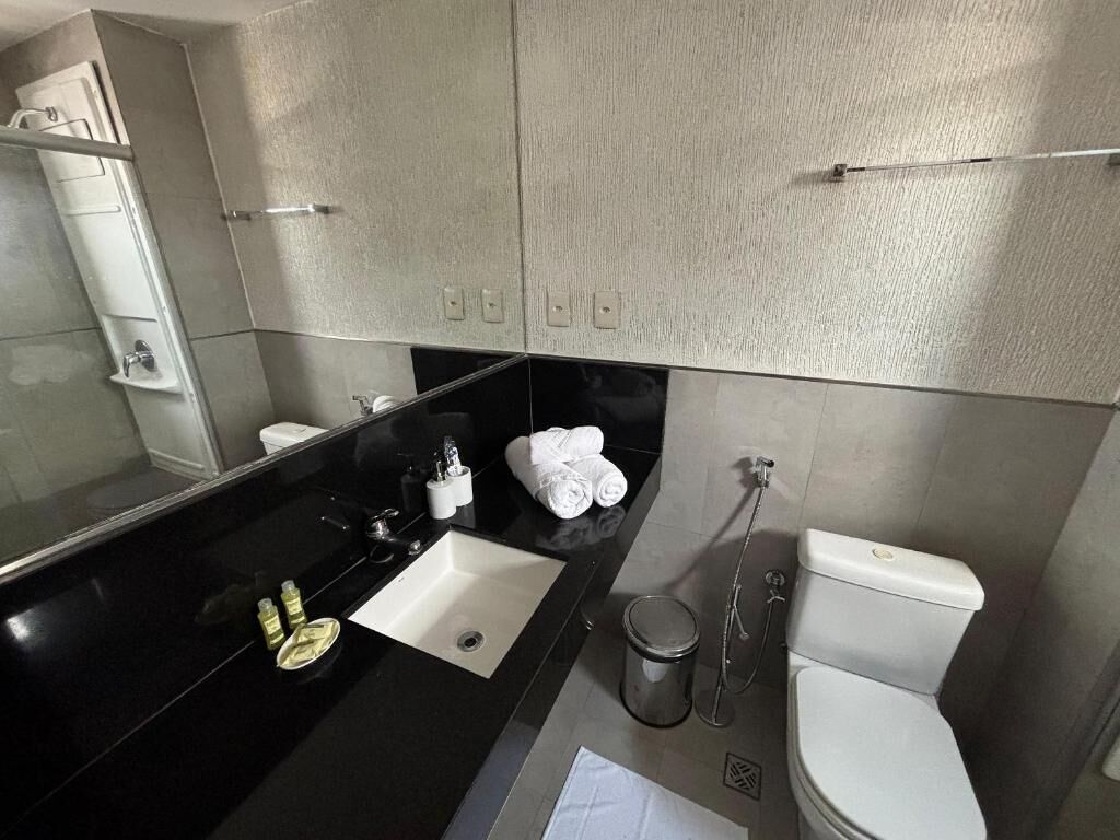 A modern bathroom with a black countertop, a white sink, a toilet, and a shower area.
