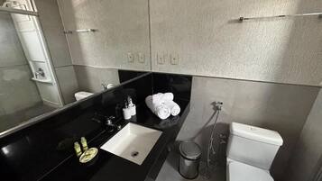 A modern bathroom with a black countertop, a white sink, a toilet, and a shower area.