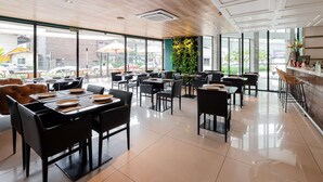 Ein geräumiges Restaurant mit hohen Decken, großen Fenstern und einer Mischung aus Sitzgelegenheiten, darunter Tische und Sitzboxen.