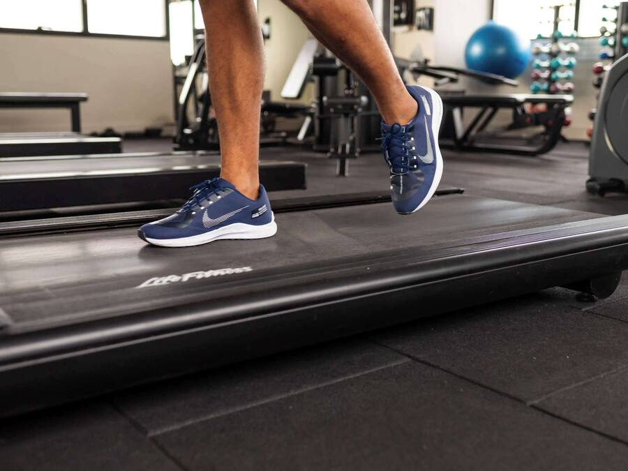 A person running on a treadmill in a gym with exercise equipment in the background.