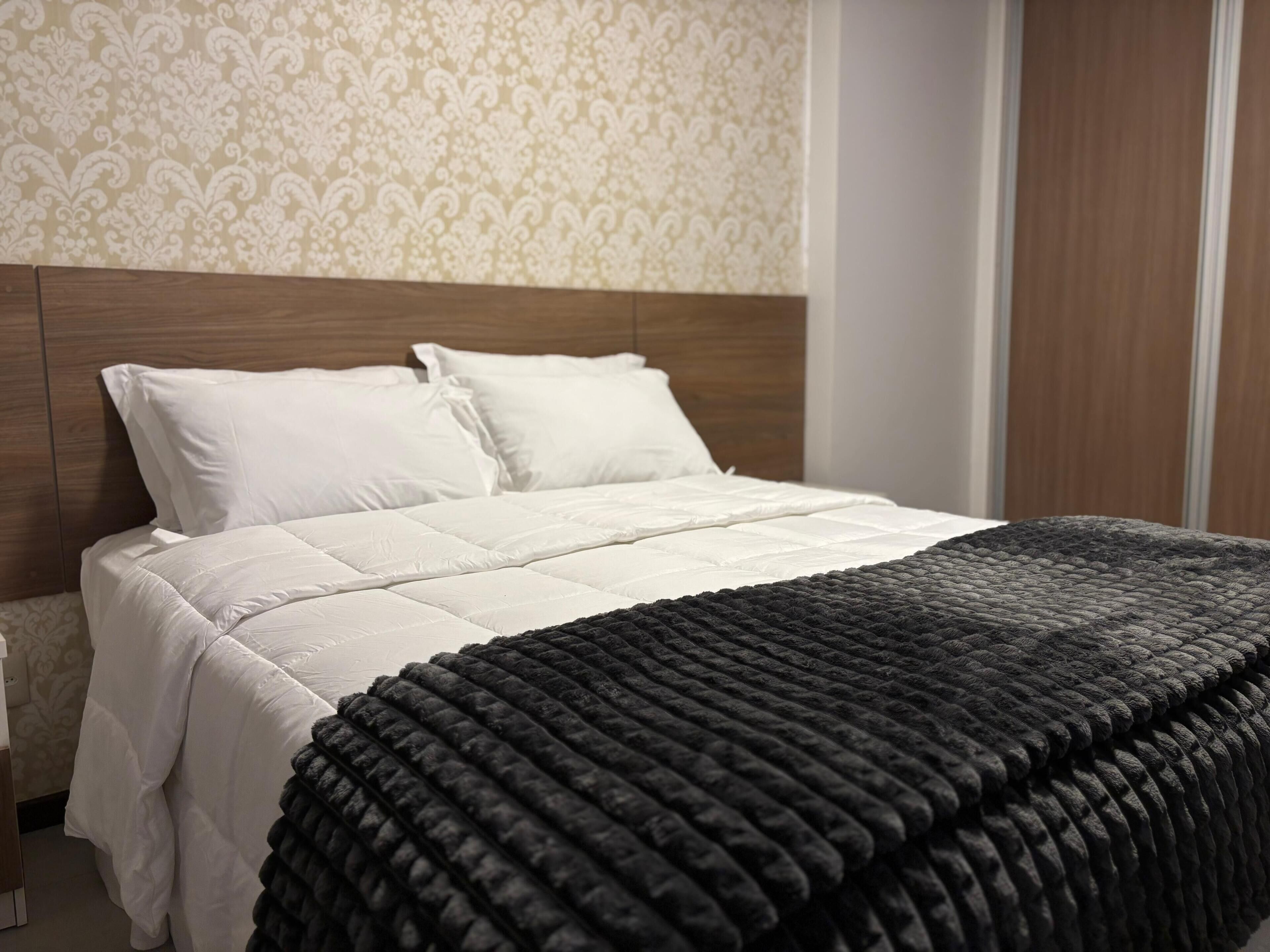 Een net opgemaakt bed met wit beddengoed en een donkere, geribbelde deken.