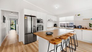 Une cuisine moderne dotée d’un réfrigérateur en acier inoxydable, de deux fours, d’un four à micro-ondes et d’un îlot central en bois avec des tabourets de bar.