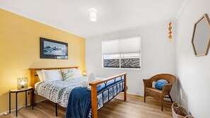 Une chambre à coucher avec un lit, une chaise, une fenêtre avec des stores, un tableau au mur et une petite table avec une lampe.
