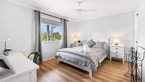 Une chambre à coucher comprenant un lit, des tables de chevet, un bureau et un ventilateur de plafond.