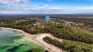 Vue aérienne d’une ville côtière avec une plage, une végétation luxuriante et un mélange de bâtiments résidentiels et commerciaux.