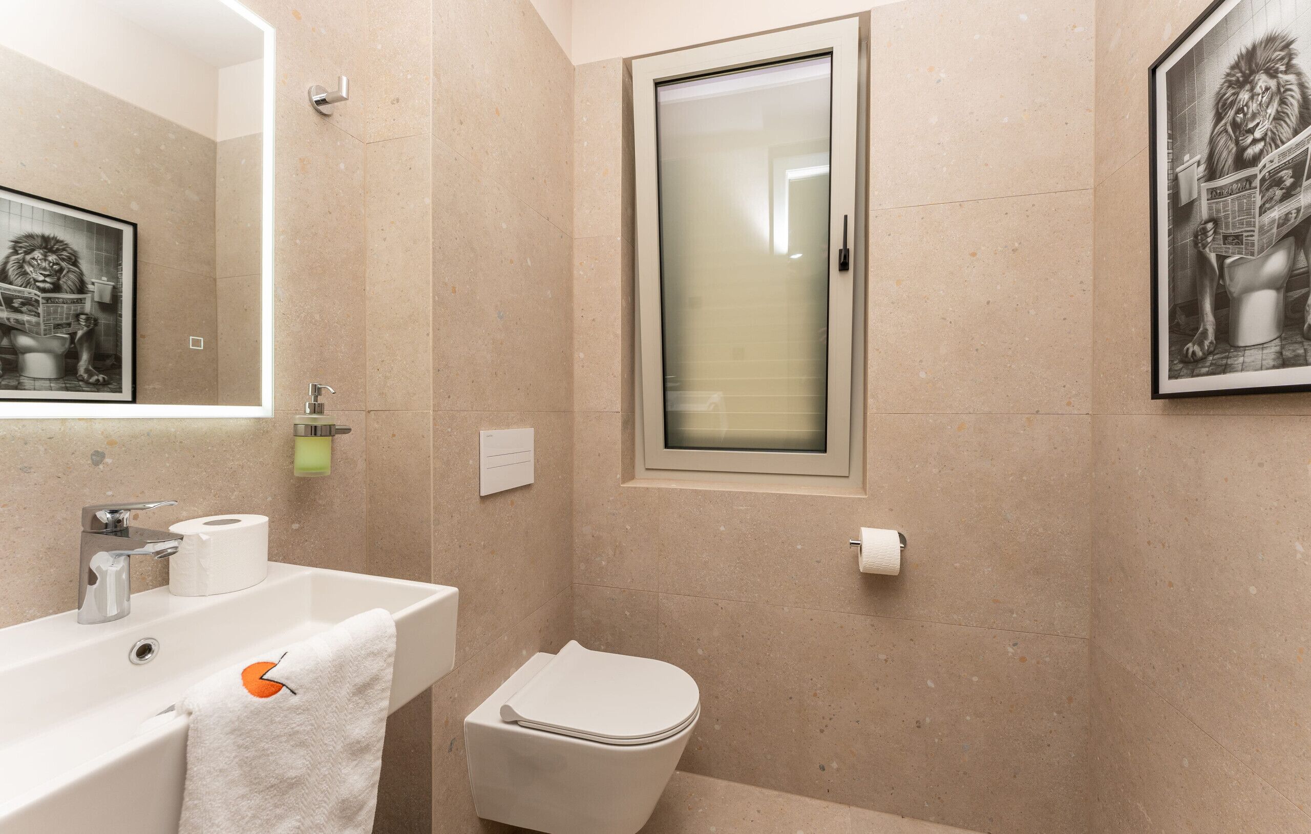 Une salle de bain avec un lavabo, des toilettes et un tableau représentant un lion lisant un journal.