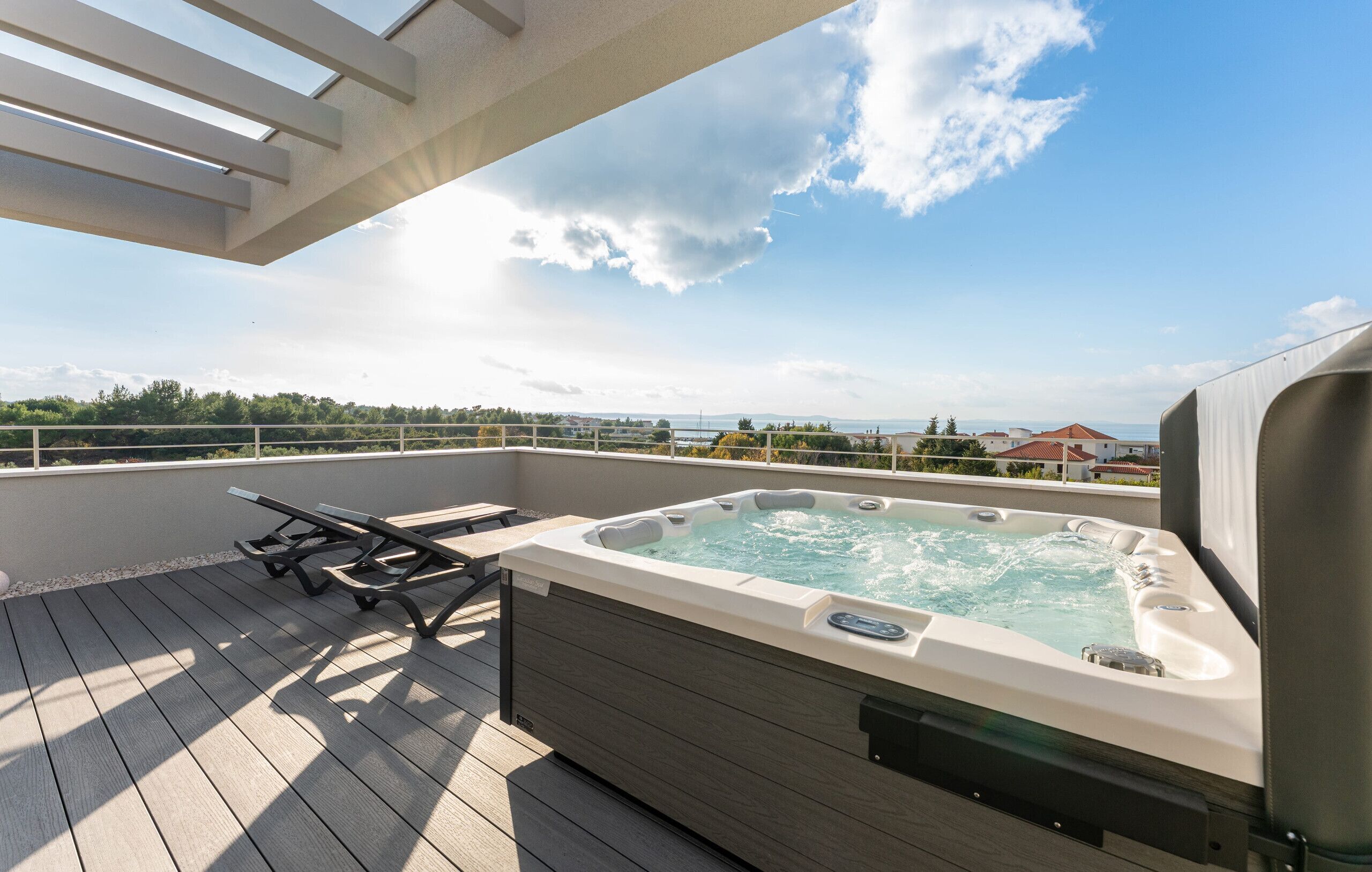 A hot tub on a wooden deck with a view of the sea and buildings in the distance.