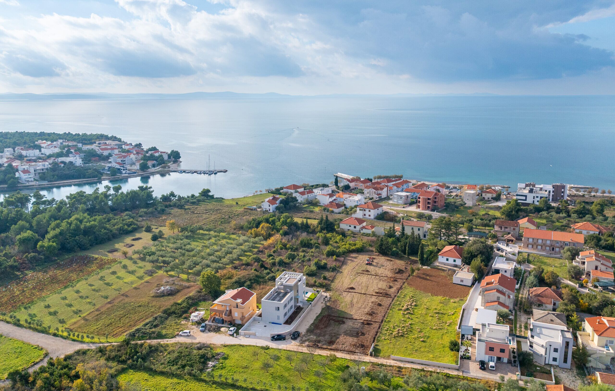 Vue aérienne d’une zone résidentielle côtière, avec des maisons, une marina et une vaste étendue d’eau.