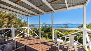 Une terrasse extérieure couverte, dotée de rampes blanches, d’un plancher en bois et de chaises en plastique blanches.