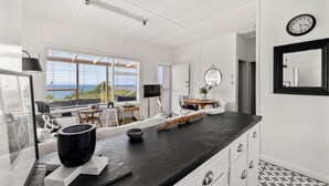 A modern kitchen with a black countertop, white cabinets, and a view of the ocean through large windows. - Moon Gate at Culburra - Pet Friendly Absolute Beachfront (Culburra Beach)