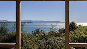 A view through a wooden-framed window overlooking a body of water with distant landforms, surrounded by dense greenery.