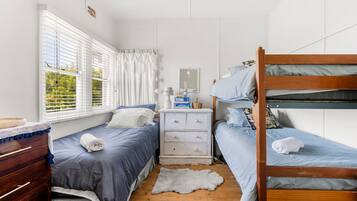 A dorm-style room with bunk beds, a dresser, a desk, and a window with blinds.