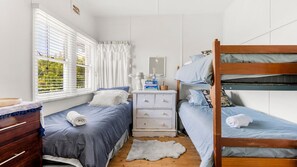 A dorm-style room with bunk beds, a dresser, a desk, and a window with blinds.