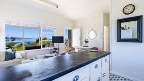 Une cuisine moderne dotée d’un grand îlot central, d’un coin repas avec une table ronde et offrant une vue sur la mer grâce à de grandes fenêtres.