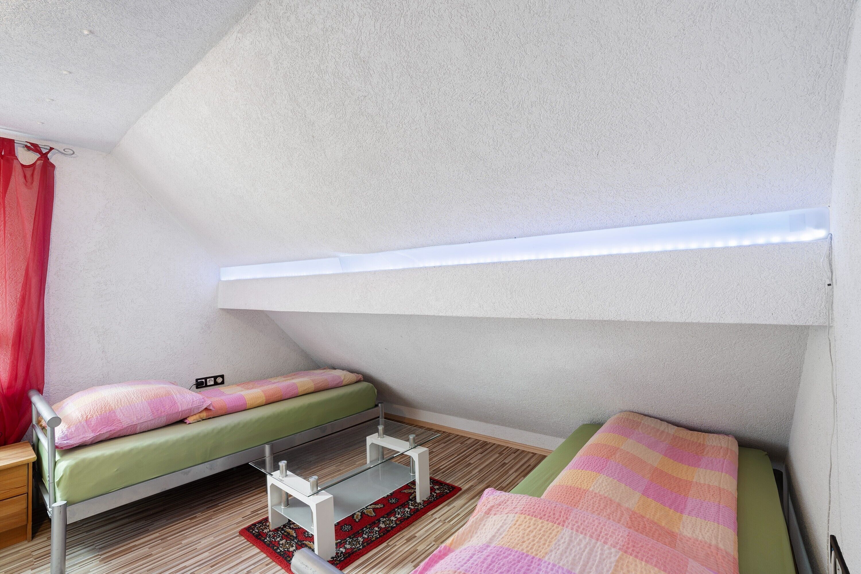 A small, triangular room with a bunk bed, a desk, and a window with a light fixture.