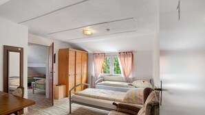 A bedroom with two beds, a wooden wardrobe, a desk, and a window with curtains.