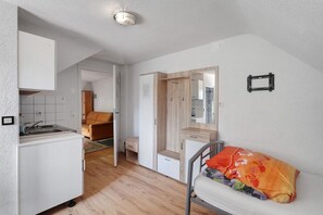 A compact room with a kitchenette, a bed with a colorful blanket, a wooden wardrobe, and a mirror.