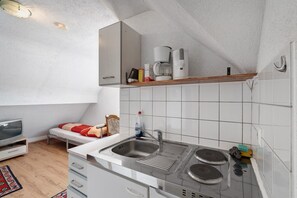 A compact kitchen with a sink, stove, and a shelf above the counter.