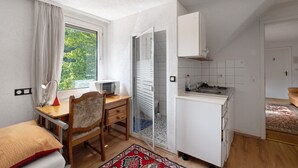 Ein kleines Zimmer mit Bett, Schreibtisch mit Stuhl, Küchenzeile und Badezimmer mit Dusche.