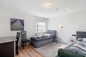 A bedroom with a bed, bedside table, lamp, window, and a painting on the wall.