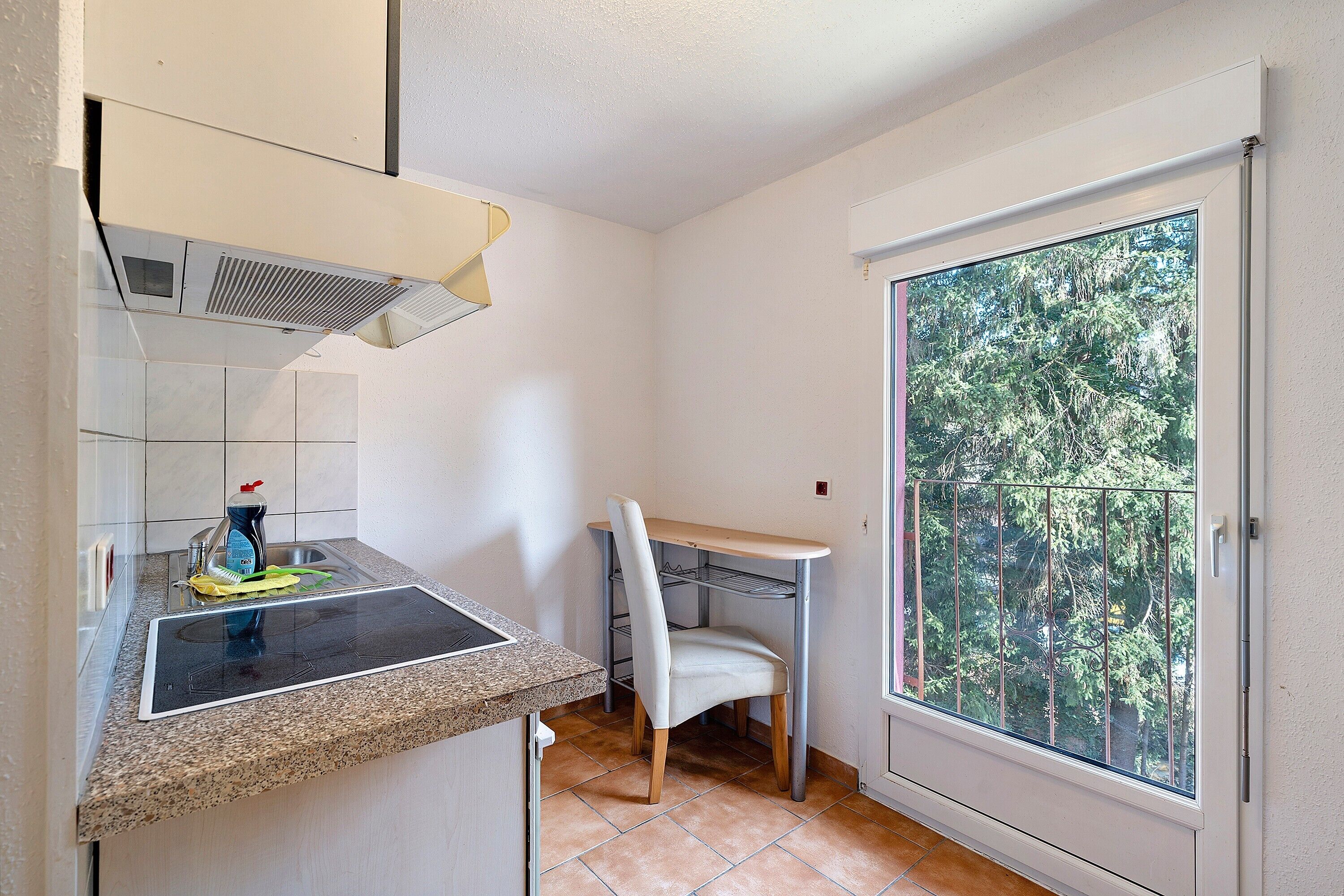 A kitchen with a built-in stove, a chair, and a window with a view of trees.