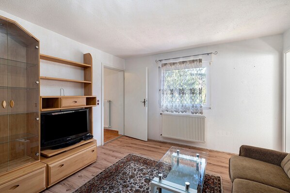A living room with a TV, wooden furniture, a glass coffee table, and a window with a curtain. - Apartment '4' with Shared Terrace and Wi-Fi (Baden-Baden)