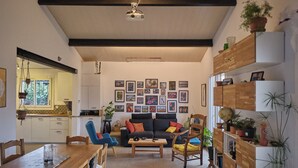 Una sala de estar acogedora con un sofá, una mesa de centro y sillas. Hay una mesa de comedor con sillas y una zona de cocina con armarios y una ventana.