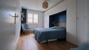Un dormitorio con cama, una silla, armario y ventana.