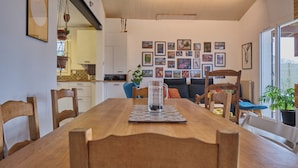 Un comedor con una mesa de madera, sillas y una taza de vidrio. Hay cuadros en la pared y una planta en la esquina.