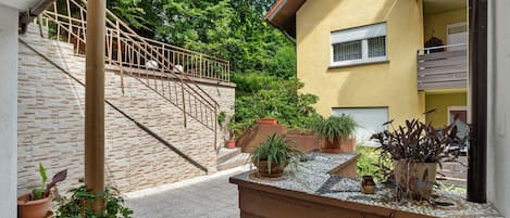 A residential building with a staircase leading to a balcony, potted plants, and a window with a white blind.