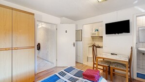 Quarto com cama, escrivaninha, cadeira, televisão e guarda-roupa.